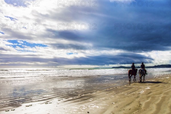 KOEKOKHE BEACH, SOUTH ISLAND, NEW ZEALAND - MARCH 15, 2018: The huge round stone boulders Moeraki. Pair of horsemen riding along the edge of the surf. The concept of ecological tourism