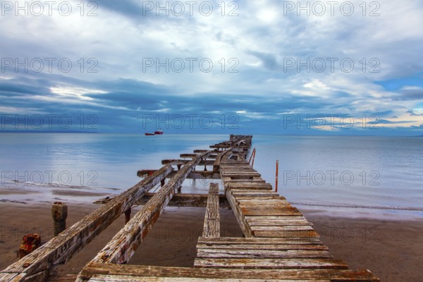 South America. Ruined ocean pier in Punta Arenas. The wooden dock flooring collapsed and rotted. Strait of Magellan. The famous Tierra del Fuego is visible on the horizon