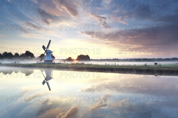 Golden sunrise over windmill reflected in river, Netherlands