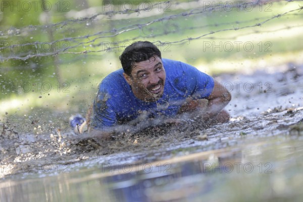 Sofia, Bulgaria - July 9, 2016: A participant is crawling through water under electrified wires at the Legion Run extreme sport challenge near Sofia. The sports event is mud and obstacle course designed to test people's physical strength, stamina, and mental grit