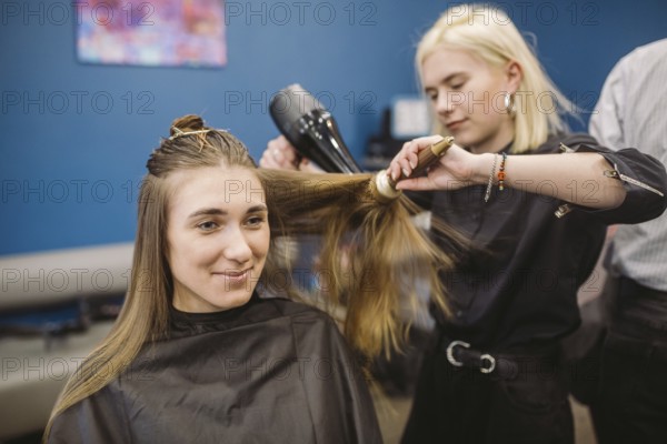 Portrait of happy woman at the hair salon. Professional hair styling concept. Hairdresser drying girl long hair using hairdryer and brush. Drying With Blow Dryer