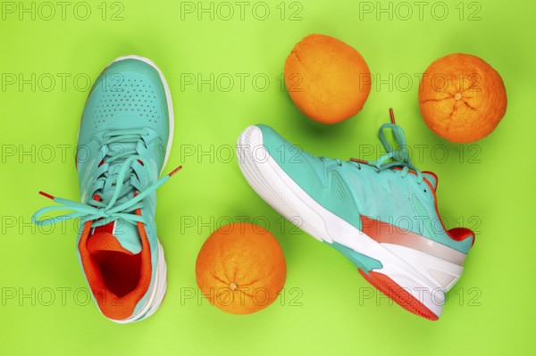 Red, cyan, white pair of new tennis shoes in studio shot over green background with oranges next to them. Directly from above
