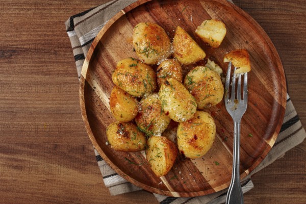 Half-eaten fried new potatoes, with butter and dill, on a wooden plate, with a fork, at home, without strangers