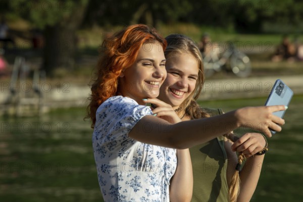 Two friends happily taking a fun selfie by the water on a sunny day, capturing joyful moments of laughter