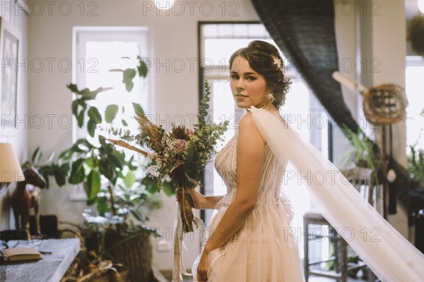 Stylish bride posing at window in light on background. rustic wedding concept. happy bohemian newlyweds. morning preparation. Young beautiful bride in boho style. Bride waiting for the big moment
