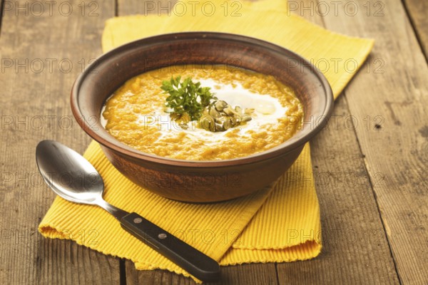 Pumpkin soup in clay bowl with spoon on the table