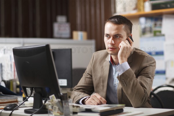 Businessman sitting behind his desk in the office talking on a mobile phone listening to the conversation with a serious expression