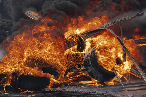 Burning automobile tires, strong flame of red fire and clouds of black fumes in sky. Selective focus, blur from strong fire