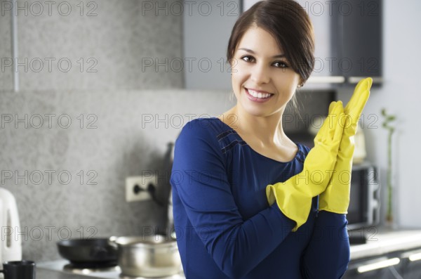 Portrait of young attractive caucasian brunette housewife at kitchen wearing the yellow rubber gloves