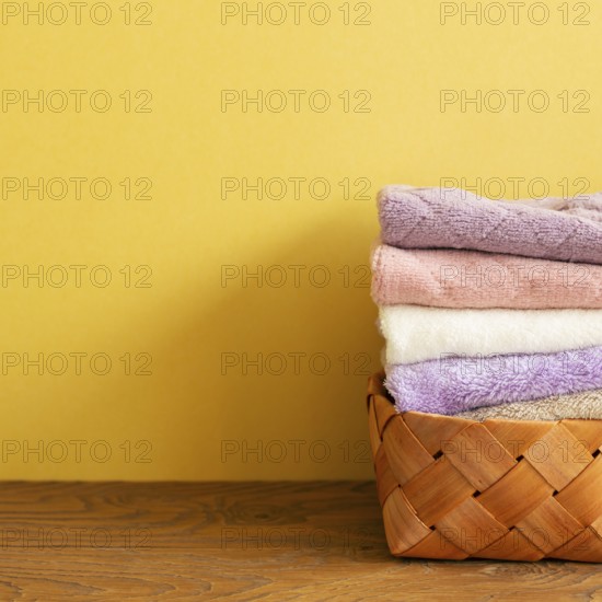 Stack of bath towels in basket on wooden table. yellow background. copy space