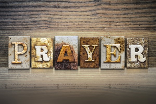 The word PRAYER written in rusty metal letterpress type sitting on a wooden ledge background