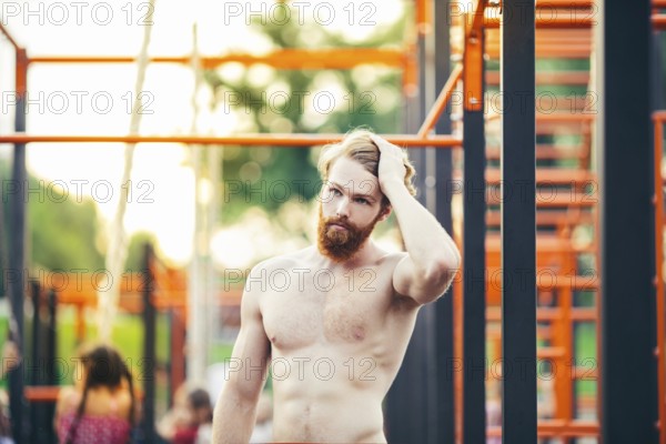 Subject sport street workout Handsome young caucasian man with a bare-chested muscular with long red hair and beard posing outdoor sports ground, gym outdoors. Sexy guy touches his hair