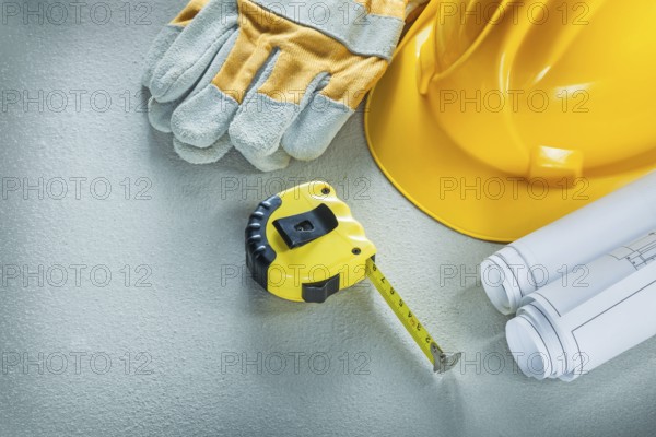 Set of blueprints building helmet protective gloves measuring tape on concrete background