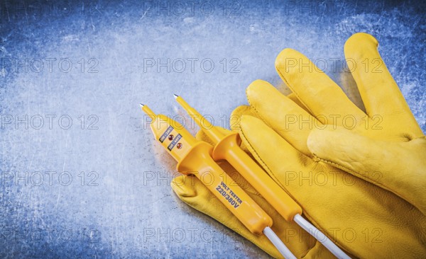 Yellow electrical tester protective gloves on metallic background electricity concept