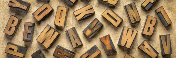 Random letters overhead background - vintage letterpress wood type of different fonts (inverted image) against brown handmade bark paper, panoramic banner