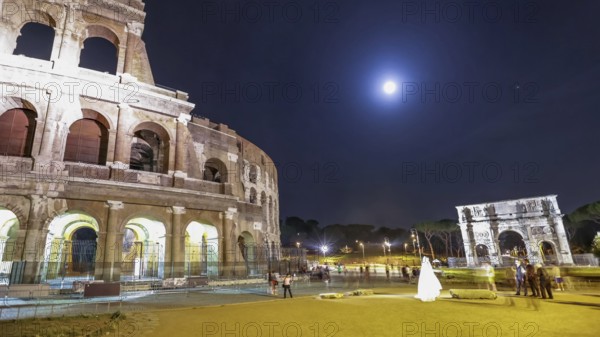 Roman Colosseum and Constantine Arch by night with tourists and photographers with a bride for marriage night photo shooting in Rome, Italy