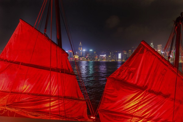 Close up of red-sail junk boat with Hong Kong island skyline background seen from the waterfront of Tsim Sha Tsui in Kowloon