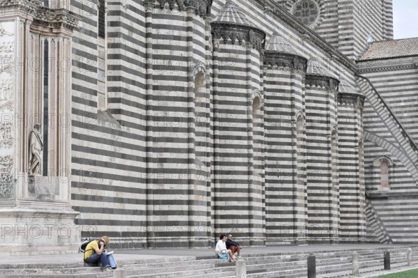 The Cathedral Basilica of Santa Maria Assunta, Orvieto, Terni, Umbria, Italy, People sitting in front of a wall of a historic striped building, Orvieto, Italy