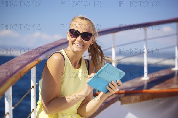 Young smiling woman in sunglasses holding tablet computer and looking somewhere while traveling by ship