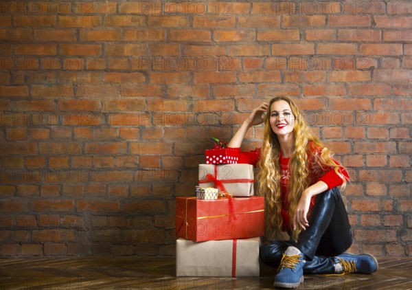 Young woman with Christmas gift near brick wall