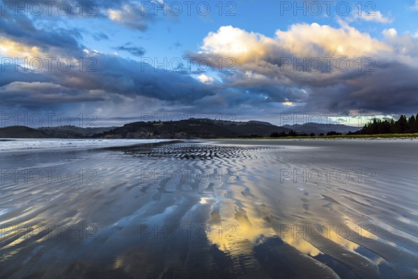 Low tide. Strips of sand and water left by the ocean tide. Sunrise over the ocean. New Zealand, Pacific Coast. The concept of artistic photography. Artistic postal and greeting card