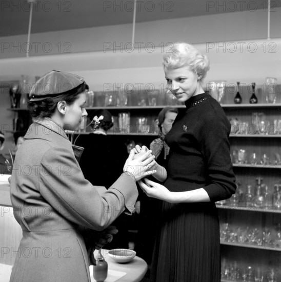 Shopping in the 1950s. A young woman in a store where a sales woman is presenting some of the stores selection of fine cermaics and decorative items designed by the famous designer Stig Lindberg. She is seen holding a vase in her hands showing it properly for the female customer. 1956 Conard ref 3181