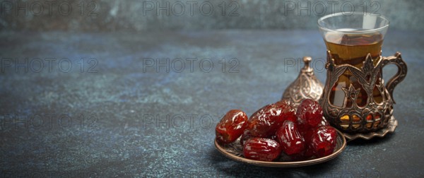 Breaking fasting with dried dates during Ramadan Kareem, Iftar meal with dates and Arab tea in traditional glass, angle view on rustic blue background. Muslim feast, space for text, food photography, food photography