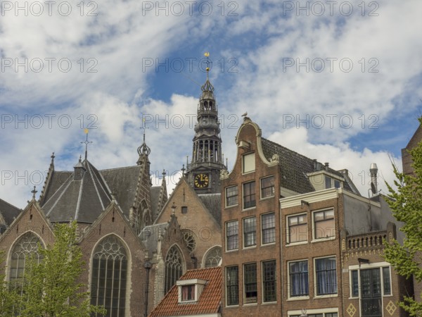 A church with a distinctive clock tower towers over historic buildings under a partly cloudy sky, Amsterdam, Netherlands