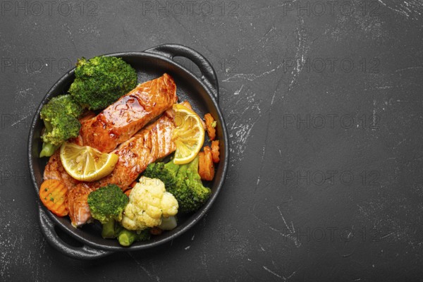 Healthy baked fish salmon steaks, broccoli, cauliflower, carrot in cast iron casserole bowl black dark stone background. Cooking a delicious low carb dinner, healthy nutrition, food photography, food photography