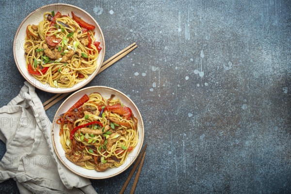 Two bowls with Chow Mein or Lo Mein, traditional Chinese stir fry noodles with meat and vegetables, served with chopsticks top view on rustic blue concrete background, space for text, food photography, food photography