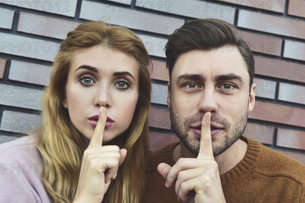 Attractive young Caucasian couple pretty woman and handsome man asking for silence, keeping index fingers on their lips, saying Shh. People, relationships, secrecy and confidential information