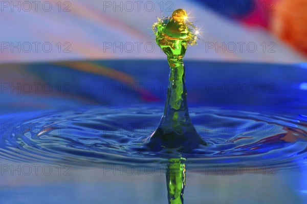 A drop of water in bright green creates a lively splashing movement on a blue water surface, Highspeed Photography, Grenzach- Wyhlen, Baden- Württemberg, Germany
