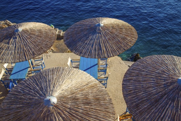 Thatched round roofs of awnings in a small cafe and water of the Mediterranean Sea on the amazing island of Hydra