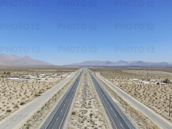 Aerial view of road in the middle of the desert under blue sky in California's Mojave desert, near Ridgecrest. Desert brush with road