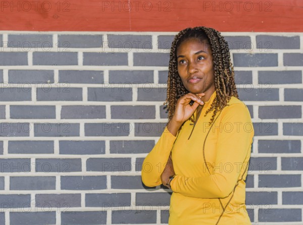 Young black woman in yellow with curly hair posing against a brick wall, Taken in Daejeon, South Korea