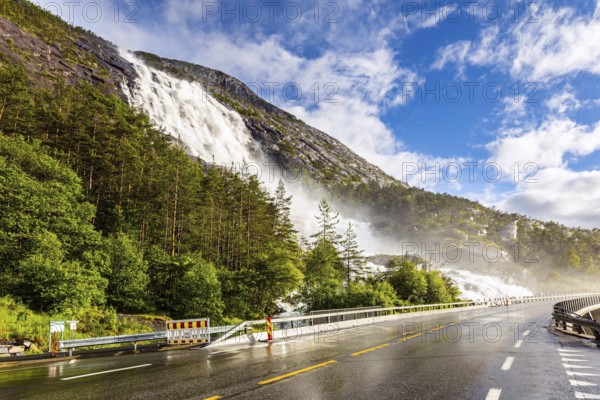 Summer cold day. The cascading Langfossen waterfall picturesquely intersects with the highway and flows into the Acre Fjord. Western Norway