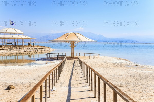 Lovely round umbrella protects from the sun. The drainless salt lake in the Middle East. Dead Sea. Coast of Israel. Railings enclose the path to the water