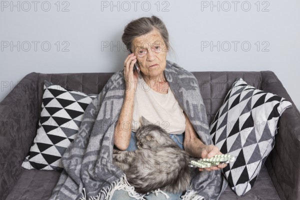 Sick senior woman taking medicine at home. Senior woman talking on mobile phone while looking at medicine in bedroom. pensioner studying medicine calling doctor while sitting on sofa with cat