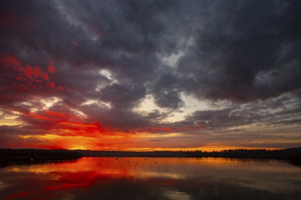 A truly stunning sunset over a calm and reflective lake showcases vibrant hues and dynamic clouds surrounding it
