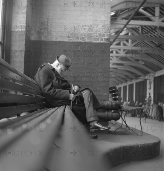 London in the 1950s. Older man sits on a bench with his pipe and stick in his knee, London 1952