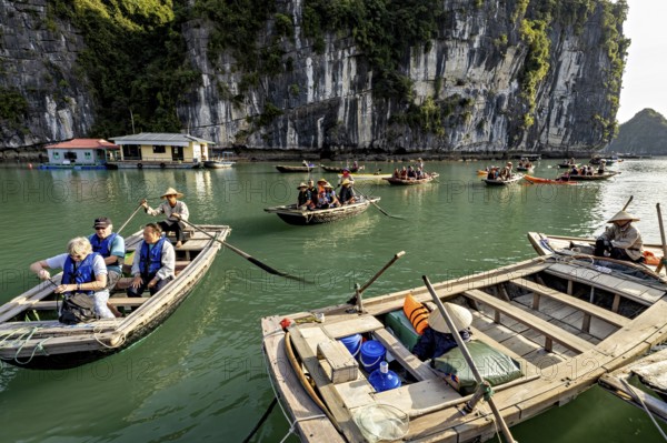 Tourists in boats enjoy a ride along a rocky shore, rowing boats for tourists in Halong Bay in Vietnam