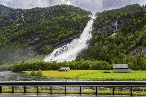Norway. Huge powerful waterfal Vidfossen. White water foam envelops the foot of the waterfall. Lush clouds and constant cold rain. Summer