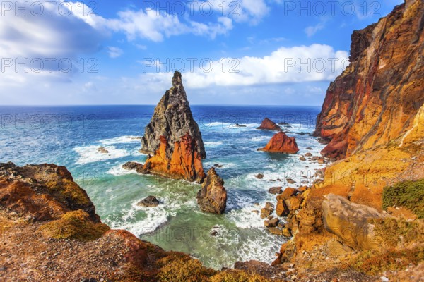 The blinding midday sun illuminates the rocky shore. Madeira is a magical island in the Atlantic. The sharp red rocks, boiling turquoise surf. The concept of active, ecological and photo tourism