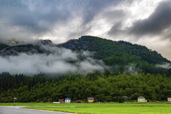 Lush green grass in the hollow. Jostedalsbreen Park. Cold summer in Norway. Valley surrounded by high forested mountains. Heavy clouds covered the sky