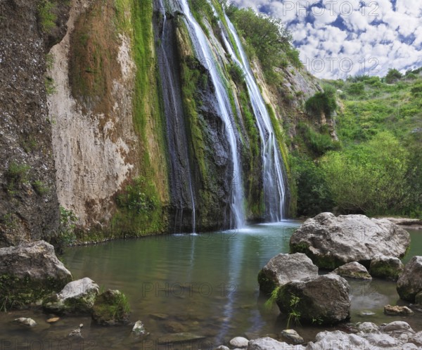 Three parallel streams of water running down the steep slope and fall in oval pool. Three-jet scenic waterfall in the mountains