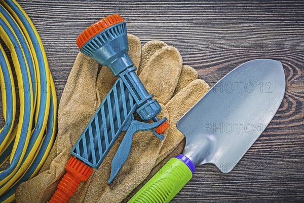 Coiled garden rubber hose leather safety gloves hand shovel on wood board gardening concept