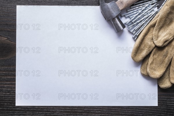 Sheet of paper metal nails claw hammer and leather safety gloves on vintage wooden board copy space construction concept