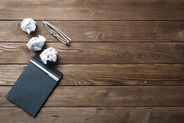Top view of well organized home office workplace. Black spiral notepad, crumpled paper and glasses on brown wooden surface. Education, creativity and working minimalist concept with copy space