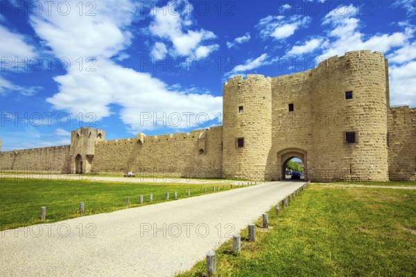 The picturesque powerful gates and fully preserved antique city walls surround the port city of Aigues-Mortes. Around the walls are green lawns. The concept of historical and photo tourism