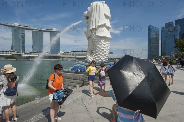 20.08.2016, Singapore, Republic of Singapore, Asia, Tourists visit the Merlion Park with the figure of the Merlion along the Singapore River in Marina Bay. The Merlion is a mythical creature and is half lion and half fish and at the same time Singapore's landmark and mascot. In the background is the striking Marina Bay Sands Hotel with its three towers